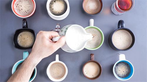 Top-down view pouring milk into assorted coffee mugs