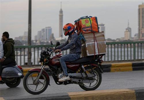 Motorcycle delivery rider hauling stacked packages over city bridge