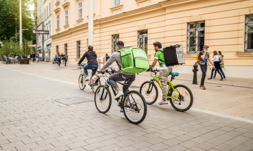 Uber Eats couriers cycling along European city sidewalk